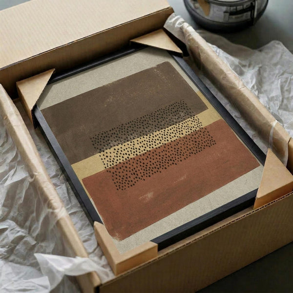 Framed abstract geometric art print featuring horizontal bands in brown, rust orange, cream, and beige tones with dotted halftone pattern overlay. The artwork is displayed in a black frame, carefully packaged in brown cardboard box with protective tissue paper and wooden dowels for safe shipping.