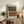 May include: Abstract geometric art print in light wooden frame displayed on rustic wooden sideboard. Features layered horizontal shapes in brown, terracotta, and cream tones with dotted texture details against light background. Styled with fern plant, ceramic vase, stacked books, and cream upholstered chair in warm-toned living room setting.