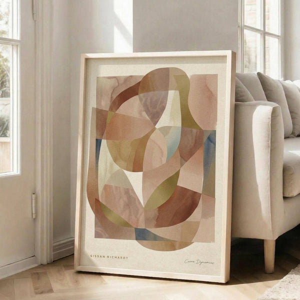 May include: Abstract geometric art print in warm earth tones featuring overlapping curved shapes in browns, tans, blues and greens, displayed in a light wood frame leaning against a beige sofa in a bright living room with white walls and large windows