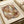 May include: Abstract geometric art print in warm earth tones featuring overlapping translucent shapes in browns, greens, and muted blues. The artwork shows curved and angular forms creating layered patterns with a watercolor-like texture. Displayed in a light wooden frame on neutral paper with an artist signature, sitting on a cream surface next to rolled paper tubes.