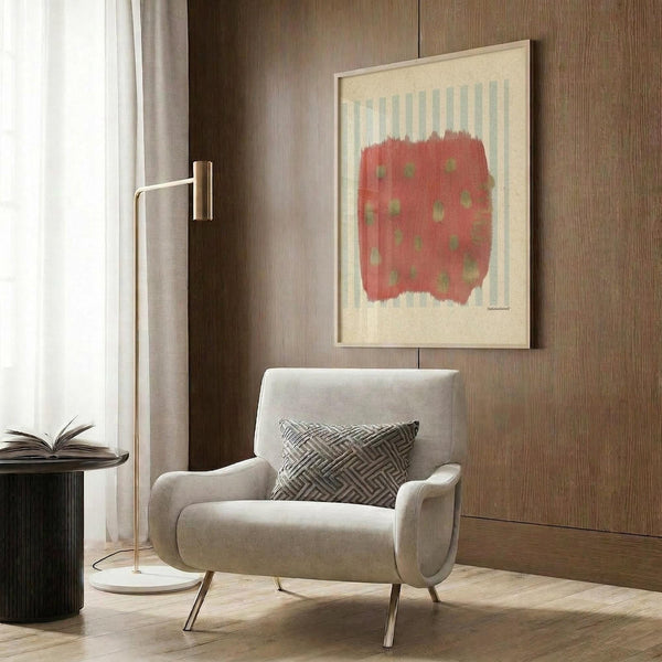 May include: Abstract art print with coral red background and sage green dots in light wood frame, displayed above beige upholstered armchair with geometric pillow. Modern reading nook with brass floor lamp, dark round side table with open book, and warm wood paneled wall.