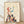 May include: Framed art print leaning against white wall on light wood floor. Features stylized illustration of figure with red flowing hair and blue arm reaching toward yellow star. Lower body transforms into colorful geometric buildings and houses in various colors including pink, blue, orange, and red. Cream background with thin wooden frame. Soft natural lighting creates gentle shadows on textured white wall.