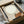 May include: Framed minimalist art print in black frame showing small figure sitting on geometric orange-brown ledge beneath large pale cream circle representing moon or sun against beige background. Print packaged in brown cardboard box with protective tissue paper and bubble wrap on white surface.