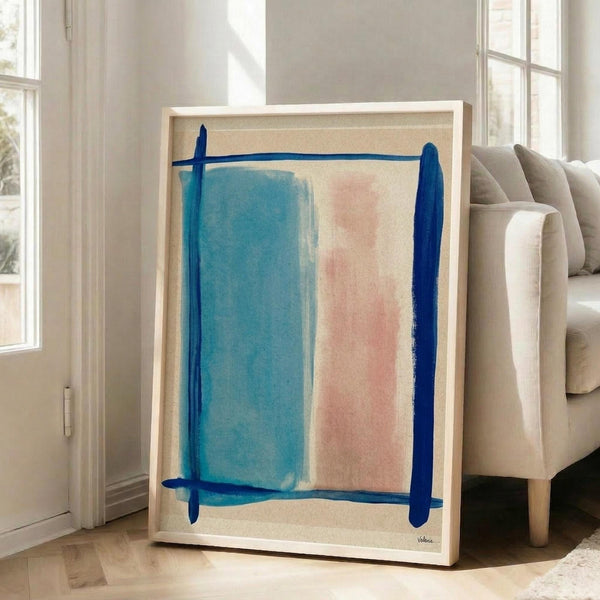 May include: Abstract art print in light wood frame leaning against white wall next to beige sofa. Artwork features soft blue and pink rectangular color blocks with bold navy blue brushstroke borders on cream background. Modern minimalist living room with large windows and natural lighting.