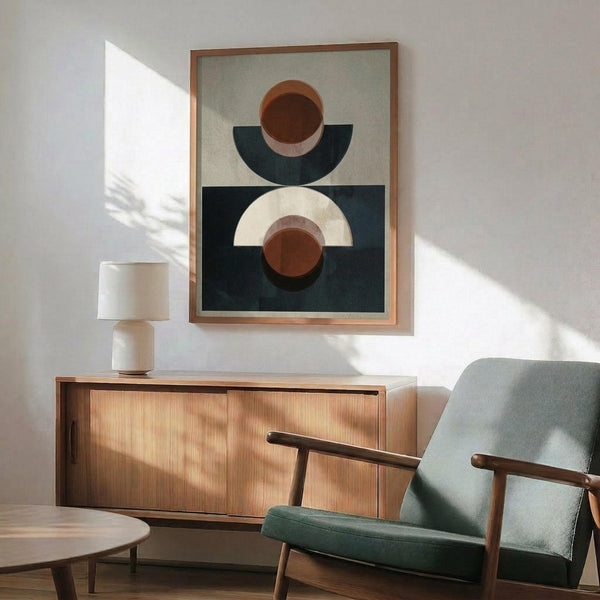 May include: Abstract geometric poster with terracotta circles and navy semicircles on sage green and dark teal backgrounds, displayed in thin wood frame above mid-century modern walnut credenza with white ceramic table lamp, next to sage green upholstered armchair with wood arms in sunlit room with white walls