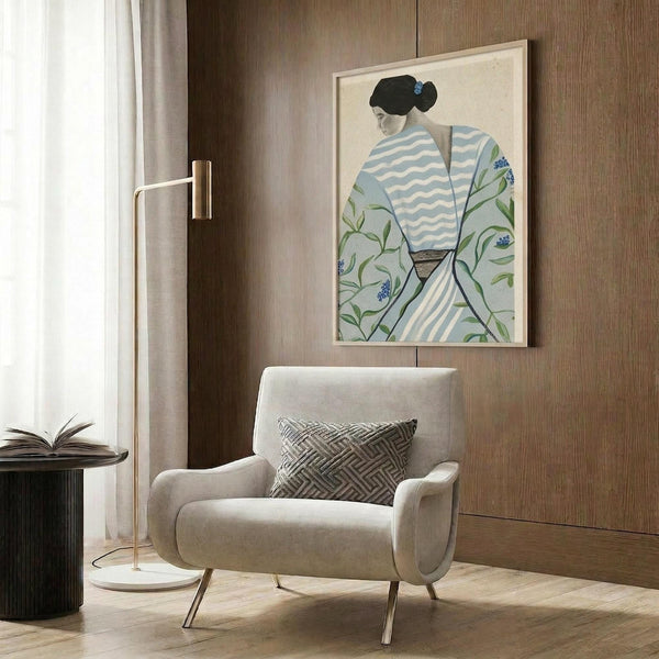 May include: Framed Asian-inspired artwork showing a woman in white and blue striped kimono with green floral pattern, displayed above a beige upholstered armchair with geometric pillow in modern living room with wood paneling, floor lamp, and side table