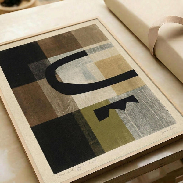 Abstract geometric artwork featuring overlapping shapes in muted tones of black, brown, olive green, cream, and gray. The composition includes curved and angular forms with textured, painterly surfaces that create depth and visual interest. The print appears on cream paper with a white border and is photographed lying flat on a neutral surface next to rolled paper, showing fine art print quality and scale.