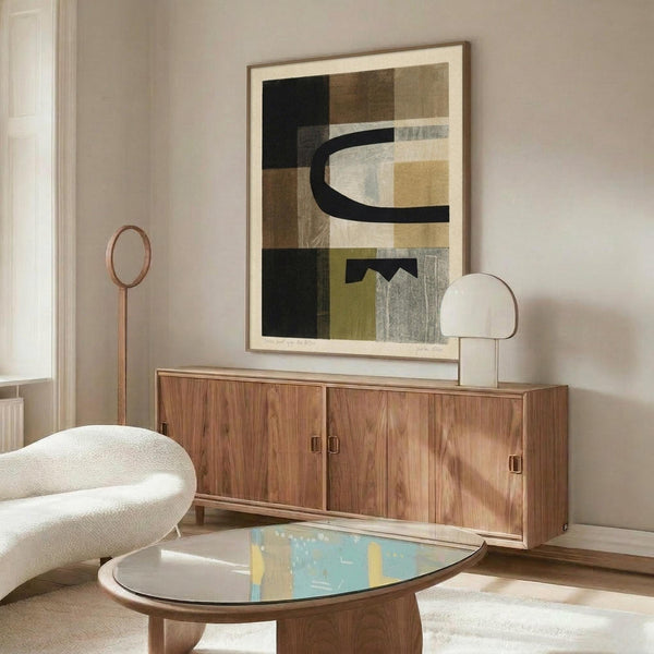 May include: Abstract geometric poster with earthy tones including black, brown, olive green, and cream blocks with curved black line, displayed in thin wooden frame above mid-century walnut credenza. Modern living room setting features white textured chair, oval glass coffee table, and minimalist table lamp on neutral walls.