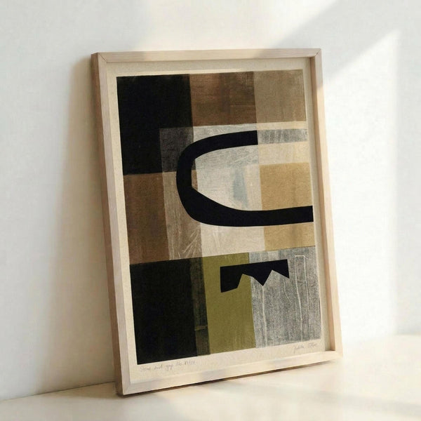Framed abstract art print featuring geometric shapes in muted earth tones including black, brown, beige, olive green, and gray. The composition shows overlapping rectangular forms with curved black lines creating organic flowing elements against angular backgrounds. The artwork is displayed in a light wood frame, leaning against a white wall on what appears to be a white surface. The print has a contemporary minimalist style with subtle textures and layered translucent effects throughout the geo