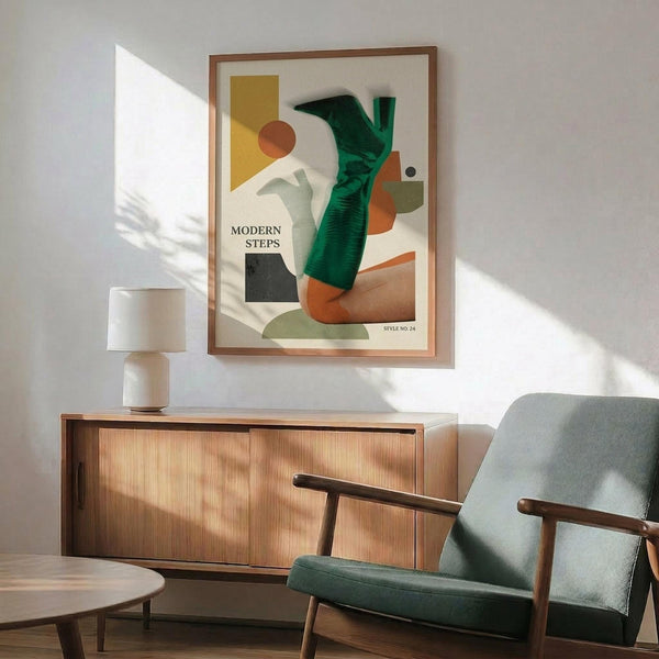 May include: Modern geometric art poster with abstract shapes in green, orange, yellow and black, featuring collaged human leg wearing green sock, displayed in wood frame above mid-century credenza with white lamp and gray upholstered armchair in sunlit room with white walls