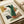 May include: Abstract geometric poster print in wooden frame featuring overlapping organic shapes in green, terracotta orange, olive, mustard yellow, gray and black. Modern minimalist artwork displayed on light wood surface with neutral wrapping paper rolls nearby. Clean contemporary styling with earth tone color palette and flowing curved forms mixed with angular geometric elements.