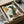 May include: Abstract art print with geometric shapes in green, orange, yellow, and cream tones, featuring curved and angular forms. Black frame displayed in cardboard shipping box with wooden frame corners and white tissue paper packaging. Print shows "MODERN STEPS" text and "STYLE NO. 24" in corner.