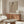 May include: Framed artwork showing a woman with dark hair in a braid wearing a leopard print garment, holding a small red bird, displayed above a wooden sideboard in a minimalist living room with cream walls, white sculptural chair, glass coffee table, and modern lighting fixtures.