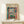 May include: Framed Henri Matisse exhibition poster featuring colorful Fauve-style painting of open window with boats visible outside and potted plants on windowsill. Poster displayed on light wood shelf with small wrapped gift box beside it. Bright blues, oranges, greens and pinks dominate the artwork within thin wooden frame against cream wall.