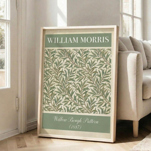 May include: Framed botanical poster with green willow branch pattern on cream background, displayed in bright living room with beige sofa, wooden floors, and large windows. Light wood frame, approximately 2-3 feet tall, leaning against white wall with natural sunlight streaming across the space.