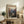 May include: Vintage-style travel poster featuring Zion National Park's dramatic red rock canyon landscape with winding river below, displayed in light wood frame on rustic wooden sideboard alongside fern plant, books, ceramic vase and table lamp in warm neutral living room setting