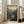 May include: Large framed vintage-style travel poster leaning against white wall next to beige armchair in bright living room. Print shows dramatic canyon landscape with towering red rock cliffs, winding river, and desert valley in warm earth tones. Wooden frame, hardwood floors, sunlight streaming through tall windows.