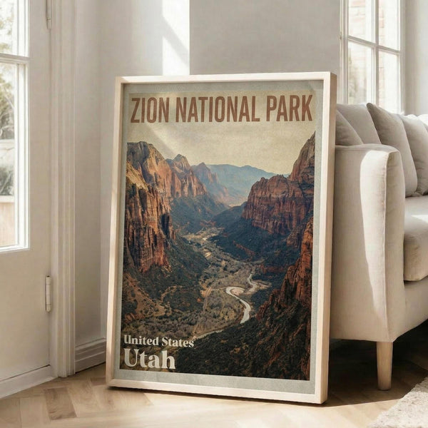 May include: Large framed vintage-style travel poster leaning against white wall next to beige armchair in bright living room. Print shows dramatic canyon landscape with towering red rock cliffs, winding river, and desert valley in warm earth tones. Wooden frame, hardwood floors, sunlight streaming through tall windows.
