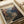 May include: Vintage-style poster print of Zion National Park featuring dramatic red rock canyon landscape with winding river below. Print shows warm earth tones and desert scenery in retro travel poster aesthetic. Displayed flat on neutral surface with white matting and rolled paper nearby, creating clean minimalist styling.