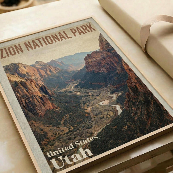 May include: Vintage-style poster print of Zion National Park featuring dramatic red rock canyon landscape with winding river below. Print shows warm earth tones and desert scenery in retro travel poster aesthetic. Displayed flat on neutral surface with white matting and rolled paper nearby, creating clean minimalist styling.