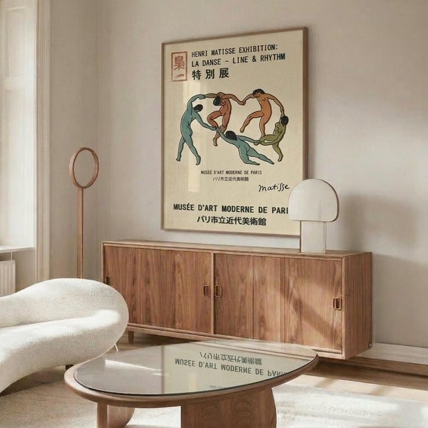 May include: Vintage-style Henri Matisse exhibition poster featuring dancing figures in green, orange and brown tones, displayed above a mid-century modern walnut credenza with sliding doors. Scene includes white curved chair, brass floor lamp, round glass coffee table, and modern table lamp. Poster shows text in English and Japanese for Musée d'Art Moderne de Paris exhibition titled La Danse - Line & Rhythm.