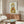 May include: Framed poster featuring a tabby cat wearing a yellow hooded raincoat and holding a red fish, displayed above a walnut wood credenza in a modern living room. The artwork has a whimsical illustrated style against a light background. Room includes a cream curved chair, oval glass coffee table, and warm neutral decor with natural lighting.