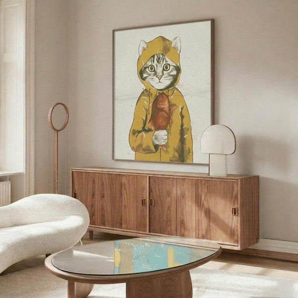 May include: Framed poster featuring a tabby cat wearing a yellow hooded raincoat and holding a red fish, displayed above a walnut wood credenza in a modern living room. The artwork has a whimsical illustrated style against a light background. Room includes a cream curved chair, oval glass coffee table, and warm neutral decor with natural lighting.