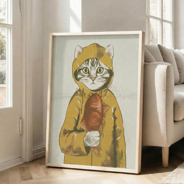 May include: Framed artwork showing a tabby cat wearing a yellow hooded raincoat and holding a red fish, displayed on wooden floor against white wall next to beige upholstered chair. The illustration has a vintage, textured appearance with muted colors on cream background in light wood frame.