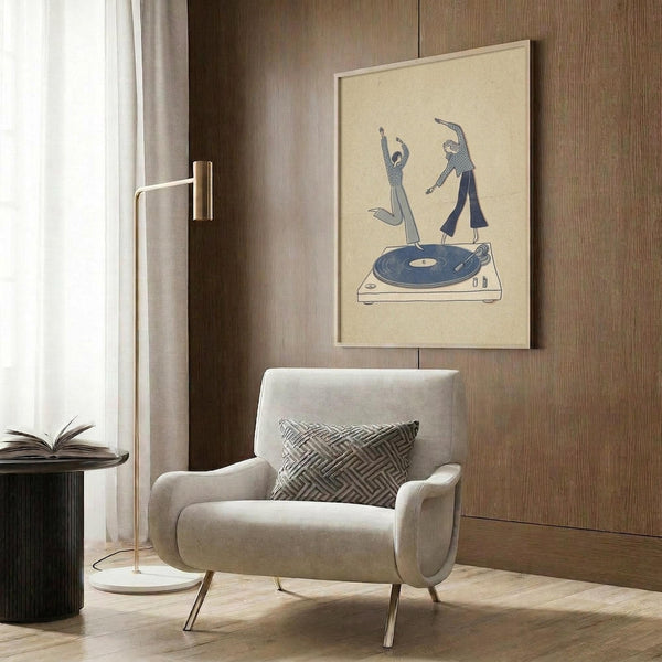 May include: Framed minimalist poster print hanging on wood-paneled wall showing two dancing figures on top of a turntable with blue vinyl record. Cream-colored background with simple line art style in blue tones. Modern living room setting with beige armchair, geometric pillow, brass floor lamp, and side table with open book. Natural lighting from window with curtains.