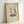 May include: Framed minimalist line art print leaning against white wall, showing two dancing figures in blue and gray tones standing on a turntable record player, displayed in light wood frame on beige textured paper background