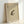 May include: Framed vintage-style Japanese ink artwork featuring a spotted frog with detailed shading, positioned on beige textured paper with black Japanese characters and red circular seal in upper left corner, displayed in light wood frame leaning against white wall