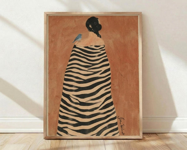 May include: Framed art print leaning against white wall on light wood floor. Orange-terracotta background with figure viewed from behind wearing black and cream striped zebra-pattern cloak or blanket. Figure has dark hair in bun with small blue bird perched on shoulder. Natural wood frame, soft lighting creates diagonal shadows on textured white wall.