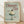 May include: Framed vintage-style poster with sage green background featuring red text reading "Dinner Club" and "The art of indulgence" alongside "A dash of decadence." Center shows retro illustration of glass coupe filled with white whipped cream topped with dark cherry. Natural wood frame sits on light wooden floor against white wall with soft window light shadows.