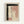 Framed abstract watercolor artwork with muted color palette featuring sage green brushstrokes forming an L-shape at top and left edges, dusty pink washes in rectangular blocks, and a vertical line of small black oval dots down the center. The piece has soft, organic edges with visible paper texture and watercolor bleeding effects. Artist signature visible in bottom right corner. Light wood frame against white wall.