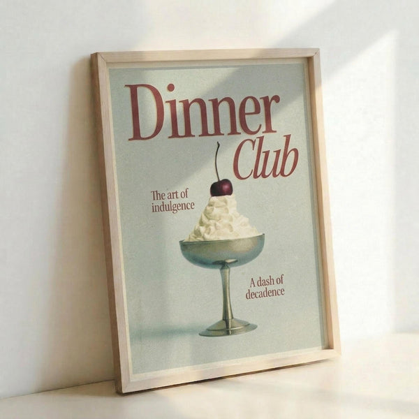 May include: Framed vintage-style poster with cream background featuring red text "Dinner Club" and "The art of indulgence." Central image shows an elegant coupe glass filled with white whipped cream or ice cream topped with a dark cherry. Additional text reads "A dash of decadence." Light wood frame sits against white wall with natural lighting creating soft shadows.