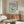 May include: Framed vintage-style poster with light blue background showing dessert in green glass bowl topped with whipped cream and cherry, red text reading "Dinner Club" and "The art of indulgence" and "A dash of decadence". Displayed above walnut wood credenza in modern living room with white sculptural chair, round glass coffee table, brass floor lamp and table mirror.