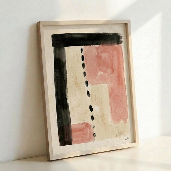 May include: Framed abstract artwork leaning against white wall, featuring bold black brushstrokes forming an L-shape, soft pink watercolor washes, and vertical line of black dots on cream paper, displayed in light wood frame with natural lighting casting gentle shadows