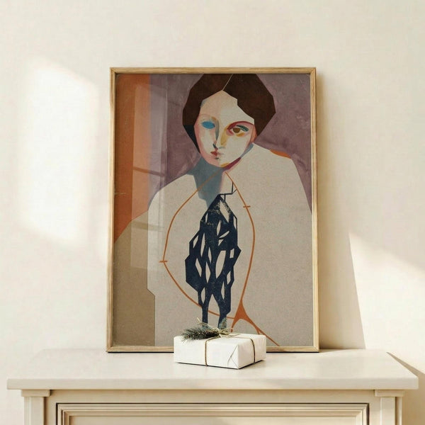 May include: Framed modernist portrait print displayed on light wooden shelf against white wall. Artwork features stylized figure with asymmetrical face in muted tones of purple, orange, and navy blue, rendered in geometric cubist style. Natural wood frame complements minimal setting with small wrapped gift box nearby.