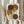 May include: Person holding framed abstract art print featuring overlapping circles in earthy tones of brown, rust orange, mustard yellow, and cream with dotted patterns running vertically through the composition. Light wood frame against neutral wall with dried pampas grass visible to the side.