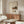 May include: Japanese calligraphy poster with kitchen still life illustrations hung above wooden sideboard in modern living room. Cream-colored print features black Japanese text, teapot, cups, and food items in minimalist style. White sculptural chair and glass coffee table visible in foreground with natural lighting creating shadows across walnut furniture.