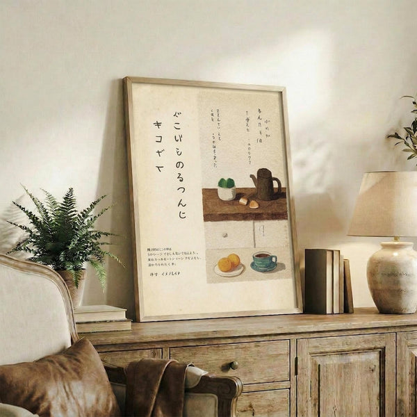 May include: Framed Japanese calligraphy poster with kitchen still life illustrations displayed on rustic wooden sideboard. Cream-colored artwork features black text, coffee pot, teacup, fruit, and kitchen items in soft watercolor style. Natural wood frame complements surrounding decor including fern plant, ceramic vase, books, and beige upholstered furniture in warm, minimalist living space with white walls.