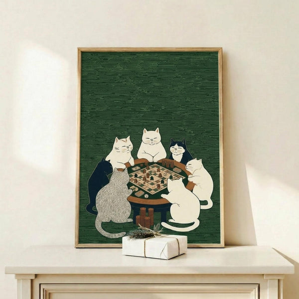 May include: Framed poster print on light wood shelf showing five cats gathered around wooden table playing board game on forest green textured background. Cats in various colors - white, gray, black, and cream - sit contentedly around chess or checkers board. Small wrapped gift package with dried botanicals sits beside frame on natural wood surface against cream wall.