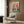 May include: Colorful penguin party poster hanging on wood-paneled wall above modern cream armchair with geometric pillow. Two cartoon penguins in Hawaiian shirts share pizza and drinks at green checkered table against coral pink background. Framed artwork displayed in contemporary living room with floor lamp and side table.