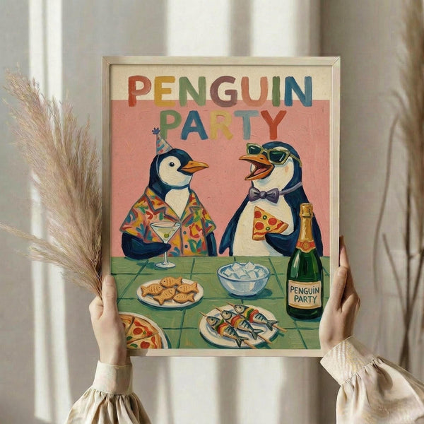 May include: Person holding framed poster showing two cartoon penguins at a party table. One penguin wears a colorful tropical shirt and party hat holding a martini, the other wears sunglasses and bow tie holding pizza. Table has fish, crackers, champagne bottle labeled "Penguin Party." Colorful "PENGUIN PARTY" text at top against pink background. Light wood frame, held against white curtained window with dried pampas grass visible.