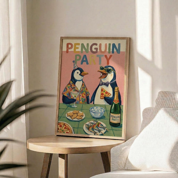 May include: Framed poster displaying two cartoon penguins at a party table with colorful "PENGUIN PARTY" text above them. One penguin wears a tropical shirt and party hat, the other has sunglasses and a bow tie. Table shows pizza, cookies, fish, drinks and champagne bottle against coral pink background. Wooden frame sits on round wooden stool next to beige chair and plant in bright, sunlit room.
