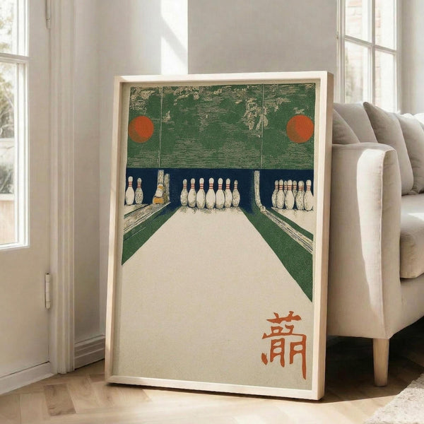 May include: Framed vintage Japanese art print depicting a bowling alley scene with green walls, cream-colored lanes, white bowling pins, and red circular elements at the top. Orange Japanese characters appear in the bottom right corner. The print is displayed in a light wood frame leaning against a white wall next to a beige upholstered chair in a bright, modern living room with large windows.