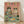 May include: Framed poster print leaning against white wall on light wood floor. Pink background with colorful "CAT PARTY" text. Two cats in sunglasses - tabby in tropical shirt holding martini, orange cat in striped dress with champagne flute. Green table displays tuna bowl, kibble bowl, cheese plate, catnip fizz bottle, and toy mice. Light wood frame with natural lighting and soft shadows.