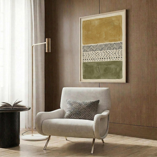 May include: Framed abstract art print displayed on wood paneled wall above modern beige armchair with geometric pillow. Artwork features ochre yellow and olive green color blocks with tribal-inspired black and white patterns including zigzags, dots, and crosses. Room setting includes brass floor lamp, side table with open book, and neutral curtains.