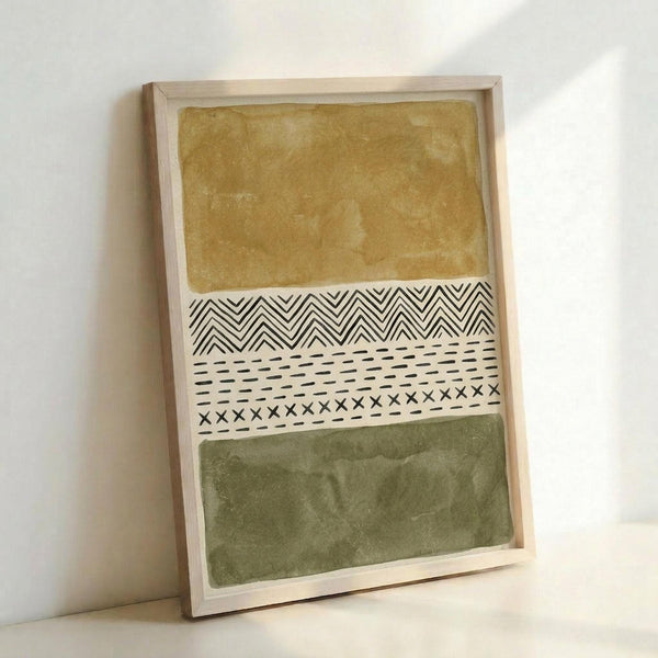 Abstract artwork featuring horizontal bands of muted ochre yellow and olive green watercolor sections separated by a white middle band with black geometric patterns including chevron zigzags, dashed lines, and small x marks. The piece is displayed in a light natural wood frame leaning against a white wall, creating soft shadows.