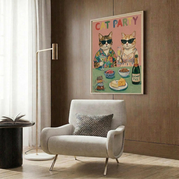 May include: Framed poster on wood-paneled wall showing two cats wearing sunglasses at a party table with colorful text "CAT PARTY" above them. The cats have drinks and food including tuna, catnip fizz bottle, and cheese. Pink and green background colors. Modern beige armchair with geometric pillow, gold floor lamp, and dark round side table with open book visible in contemporary living room setting.